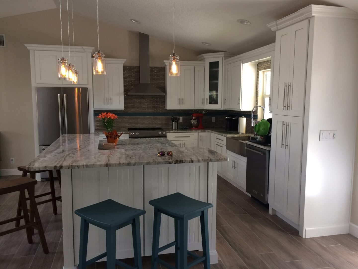 Modern kitchen with marble island, pendant lights, and teal stools.